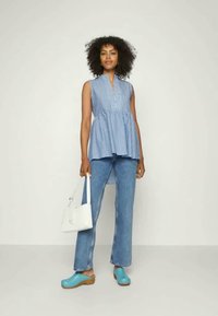 Top sem mangas listrado em azul claro com decote em V, combinado com jeans azuis, tamancos azul claro e uma bolsa branca. Conjunto casual com textura em camadas.