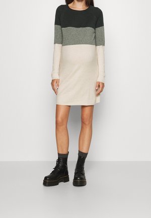 Frau trägt ein langärmeliges, farblich abgesetztes Strickkleid in Schwarz, Grau und Creme mit schwarzen Schnür-Stiefeletten und grauen Socken.