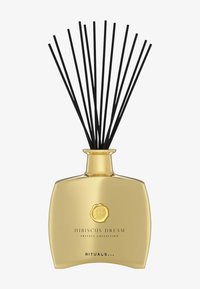 Hibiscus Dream diffuser med en gullfarget glassflaske, svarte rørepinner og et dekorativt emblem. Strømlinjeformet form, jevn overflate og elegant design.