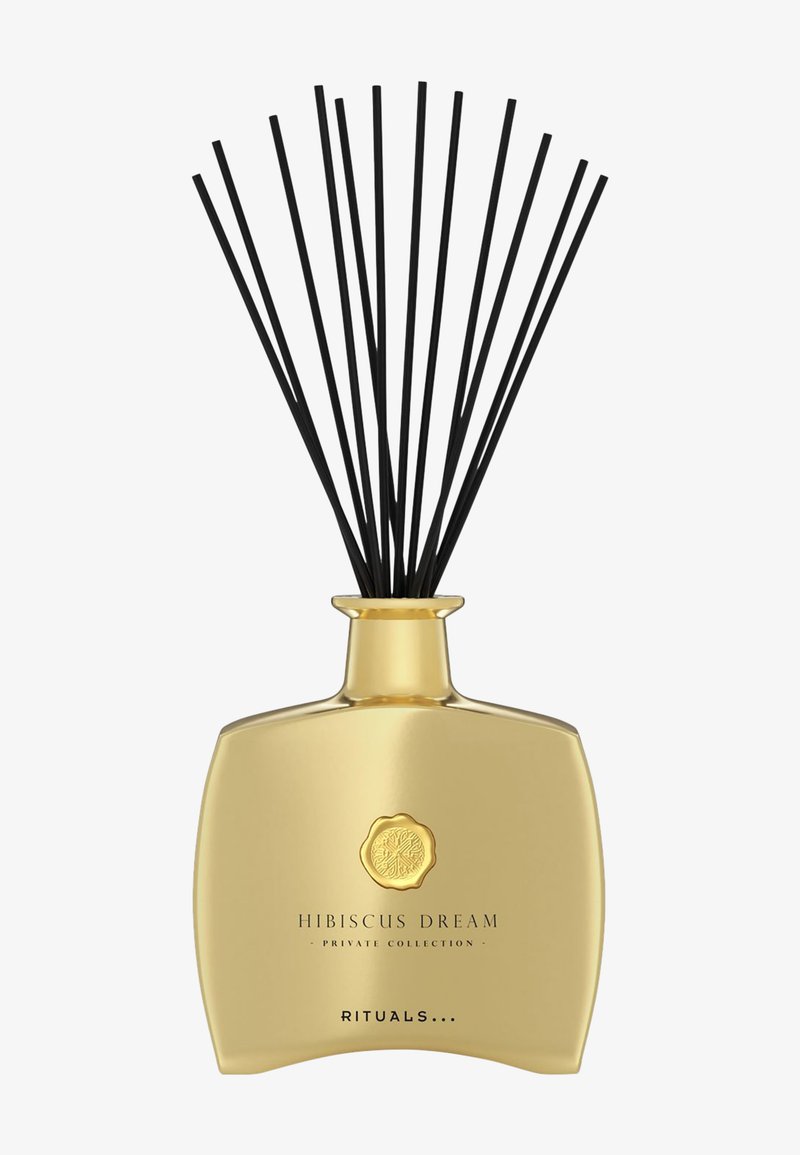 Hibiscus Dream diffuser med en gullfarget glassflaske, svarte rørepinner og et dekorativt emblem. Strømlinjeformet form, jevn overflate og elegant design.