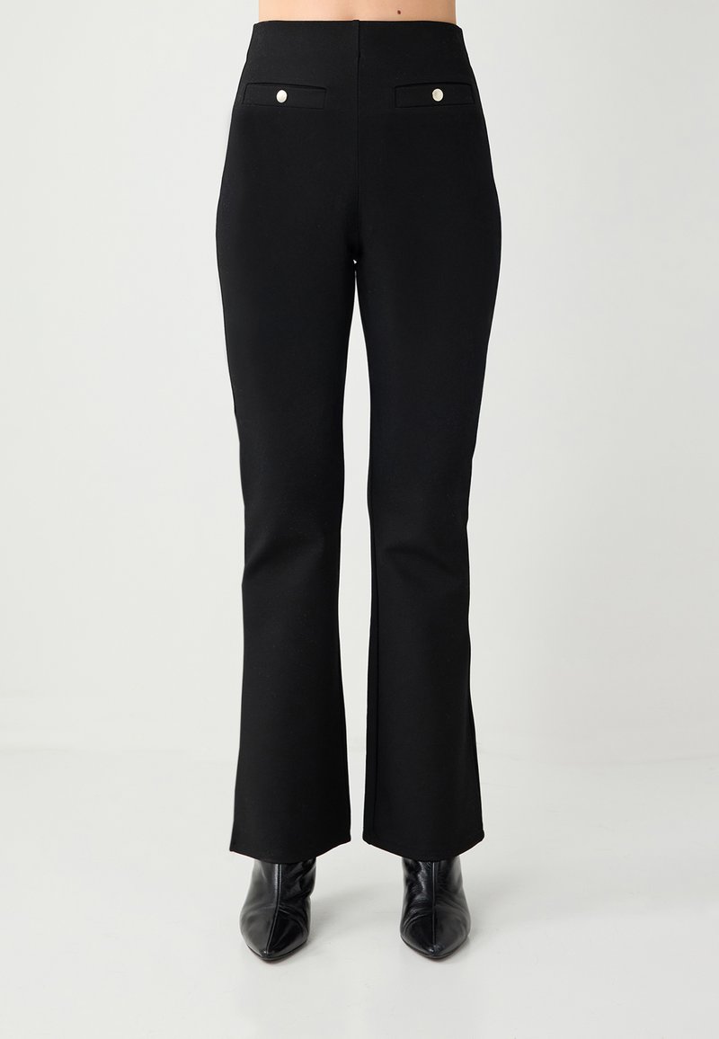 Pantalon noir évasé en tissu extensible, avec deux poches arrière ornées de boutons argentés, coupe ajustée et texture lisse.