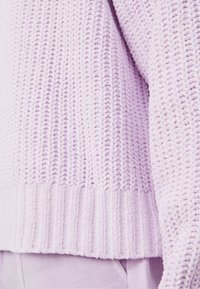 Jasnofioletowy sweter o fakturowanej strukturze z dzianinowym wzorem, z żebrowanym dołem i mankietami. Materiał wydaje się miękki i przytulny.