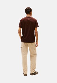 Camiseta de algodón marrón combinada con pantalones cargo beige que cuentan con bolsillos laterales y costuras de contraste, vista desde la parte posterior.