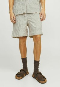 Pantalones cortos texturizados de color gris claro con cintura elástica, combinados con sandalias marrón oscuro y calcetines acanalados. Los pantalones cortos presentan un diseño arrugado.