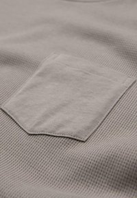 Graues Baumwoll-T-Shirt mit strukturiertem, geripptem Muster; verfügt über eine kleine, quadratische Brusttasche mit sauberem, genähtem Rand.