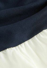 Námořnická modrá rypsová látka překrývá měkkou bílou část s nařasenou texturou, což ukazuje kontrast barev a materiálů.