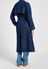 Abrigo de trench de mezclilla oscura con cintura ceñida, gran solapa y mangas largas. Presenta un diseño de espalda en capas y puños abotonados.