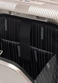 Intérieur d'une valise rigide argentée avec doublure noire rayée de blanc et marque "WITTCHEN". Comprend des compartiments et une sangle de sécurité.