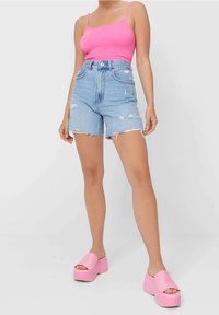 Rosa ribbad linne som kombineras med ljusblå denimshorts med hög midja, som har fransade nederkanter och slitna detaljer, kompletterat med rosa platåsandaler.