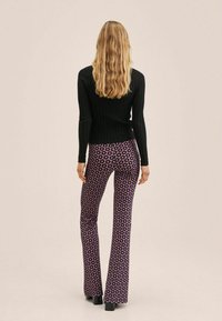 Czarny prążkowany top z długim rękawem w połączeniu z fioletowymi spodniami w kant w kwiatowe motywy, na neutralnym tle.