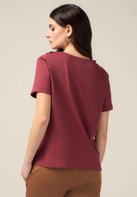Maroon Kurzarmoberteil aus weicher Baumwolle, mit lockerer Passform, umgeschlagenen Ärmeln und weitem Halsausschnitt. Glatte Textur mit minimalen Details.