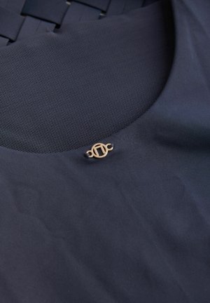 Donker marineblauwe stof met een gladde textuur bevat een netpaneel en een vergulde embleemaccent. Stijlvolle maar subtiele ontwerp elementen.