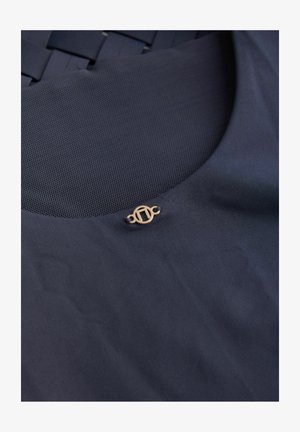 Tessuto blu scuro con una trama liscia presenta un pannello in rete e un accento emblematico in tono oro. Elementi di design eleganti ma sobri.