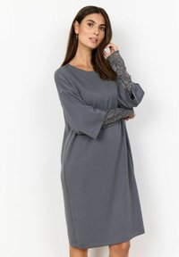 Rochie midi gri cu mâneci scurte, lejere. Accente din dantelă la manșete. Țesătură moale și netedă. Croi relaxat cu decolteu rotund.