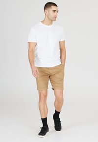 Witte korte mouwen t-shirt gecombineerd met tan opgerolde shorts. Zwarte sneakers en sokken maken de casual outfit compleet. Eenvoudig en strak ontwerp.