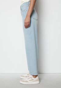 Světle modré rifle rovného střihu vyrobené z denimu, s středním pasem, zadními kapsami a čistým lemem, v kombinaci s bílými a béžovými teniskami.