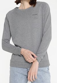 Grauer Pullover aus weichem Stoff mit Rundhalsausschnitt und langen Ärmeln. Ein kleines Logo ist auf der Brust aufgedruckt. Lässige Passform.