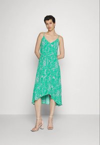 Vestido verde feito de tecido leve, com um padrão floral, alças spaghetti, decote em V e uma bainha assimétrica.