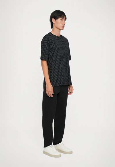 Chemise noire à manches courtes avec un motif en losange texturé, associée à un pantalon noir et des baskets blanches. Design simple et décontracté.