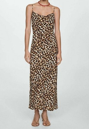 Kobieta ubrana w midi sukienkę bez rękawów w panterkowy wzór z cienkimi ramiączkami, czerwoną koralikową naszyjnik oraz beżowe sandały na otwartym palcu.