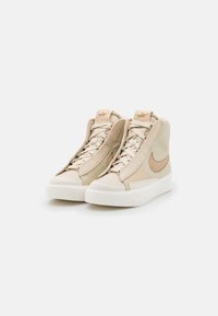 Beige höga sneakers gjorda av läder och syntetiska material, med en vit gummisula, varumärkesdetaljer och tonade skosnören.