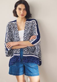 Lichtgewicht open kimono met een marineblauw en wit bladpatroon, aangevuld met horizontale strepen, gecombineerd met denim shorts.