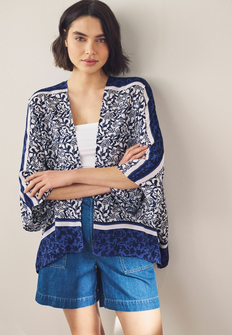 Lichtgewicht open kimono met een marineblauw en wit bladpatroon, aangevuld met horizontale strepen, gecombineerd met denim shorts.