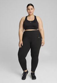 Juodas sportinis liemenukas ir aukšto liemens leggingsai, pagaminti iš elastingos medžiagos. Ant liemens ir kelnių yra logotipas. Juodi sportiniai bateliai.
