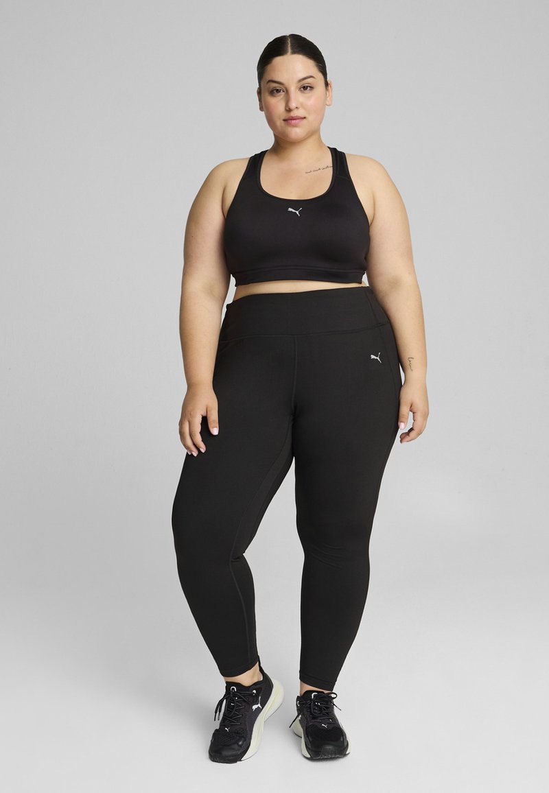 Juodas sportinis liemenukas ir aukšto liemens leggingsai, pagaminti iš elastingos medžiagos. Ant liemens ir kelnių yra logotipas. Juodi sportiniai bateliai.