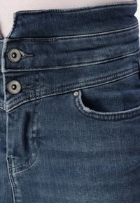 Denim jeans med en mørkeblå vask, høyt liv-design, to metallknapper i midjen, og en liten frontlomme med frynsete kanter.
