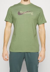 Camiseta de algodón color verde oliva con un logo y el texto "Entrenamiento" en color crema y marrón oscuro en el pecho. Manga corta, cuello redondo.