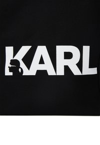 Fekete vászontáska nagy fehér "KARL" felirattal és profil sziluettel a "K" betűben. Kompakt, strukturált dizájn.
