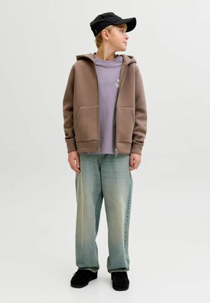 Brun lynlåstrøje med hætte, båret over en lys lilla t-shirt. Lyseblå, løstsiddende jeans og sorte sko fuldender outfittet.