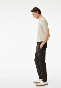 Jasno beige ryflowana koszulka polo zestawiona z ciemnymi spodniami i białymi trampkami z brązową podeszwą, skupiając się na prostym, codziennym designie.