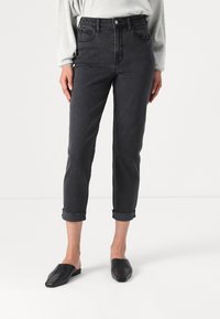 Calças de ganga pretas, cropped, com cintura alta, com punhos dobrados e design de cinco bolsos, combinadas com mules pretas de sola plana.