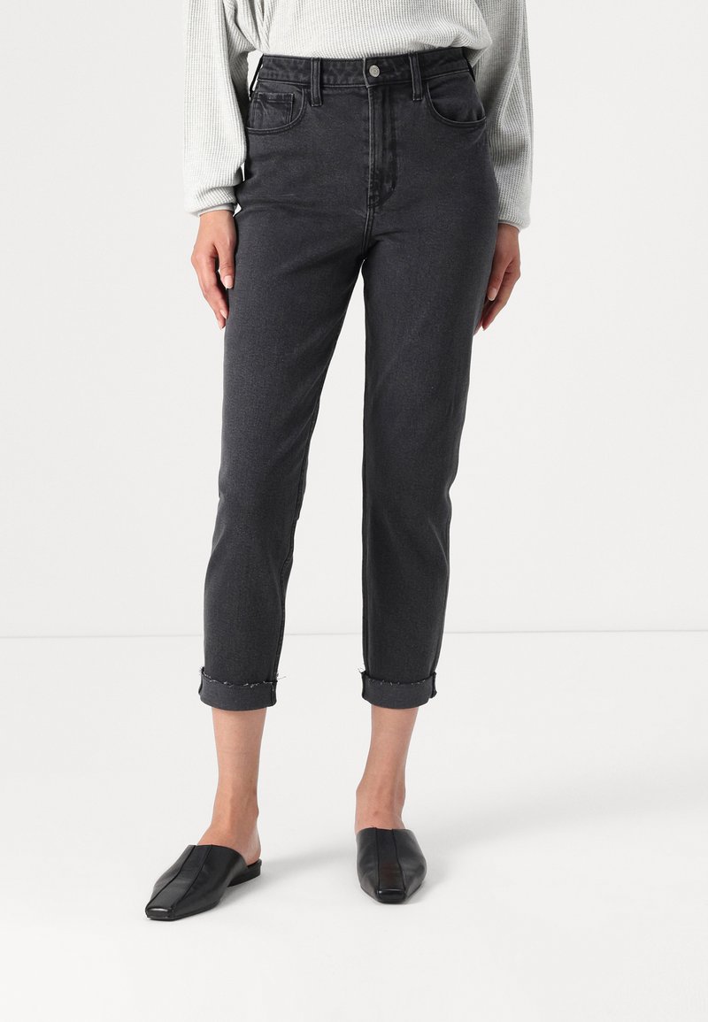 Calças de ganga pretas, cropped, com cintura alta, com punhos dobrados e design de cinco bolsos, combinadas com mules pretas de sola plana.