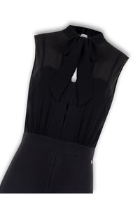 Combinaison noire avec un haut transparent sans manches et un nœud au cou. Taille plissée, fermeture éclair dissimulée et tissu lisse et mat.