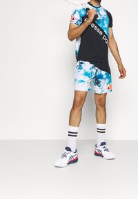 Sportovní outfit s černobílo-modrým tričkem s krátkým rukávem a odpovídajícími šortkami, doplněný bílými teniskami a pruhovanými ponožkami.