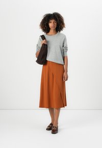 Grå langermet topp, rustfarget omslagskjørt, brun veske og mørke slip-on sko med gullakenter. Minimalistisk design, myke teksturer.
