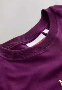 Lila Rundhalsausschnitt-Sweatshirt mit strukturiertem geripptem Kragen, das eine glatte Stoffoberfläche aufweist und ein Etikett mit Größeninformation im Halsausschnitt hat.