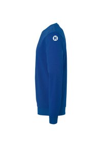 Blå sweatshirt med lange ærmer vist fra siden med et hvidt cirkulært logo indeholdende bogstavet "K" på overarmen.