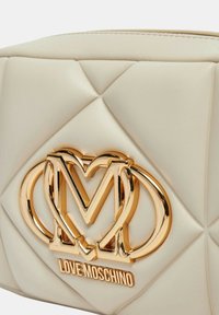 Borsa in ecopelle crema con design trapuntato, hardware in metallo dorato e chiusura con zip superiore.