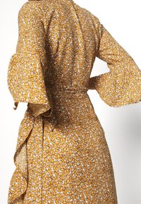 Vestido envolvente amarillo con mangas acampanadas; presenta pequeños patrones de hojas intrincadas y una cintura ajustable, hecho de una tela ligera.