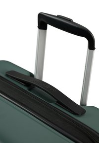 Maleta con un exterior texturizado verde, cremallera negra y asa. Cuenta con un asa retráctil metálica y un agarre negro resistente.