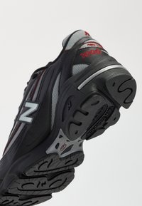 Scarpe da corsa nere e grigie con accenti rossi, tomaia in rete e suola in gomma testurizzata con un caratteristico motivo del battistrada.