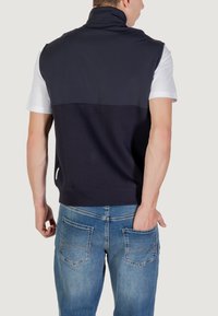 Top senza maniche di colore navy con colletto alto e una T-shirt bianca sotto; abbinato a pantaloni in denim azzurro chiaro con due tasche posteriori.