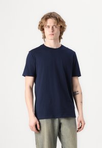 Camiseta de algodón color azul marino con un cuello redondo clásico, mangas cortas y una textura suave. Combinada con pantalones de mezclilla claros.