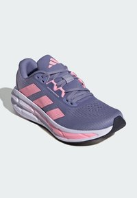 Chaussure de sport violette avec des accents roses, tige en mesh, superpositions texturées et semelle rembourrée. Présente le logo à trois bandes sur le côté.