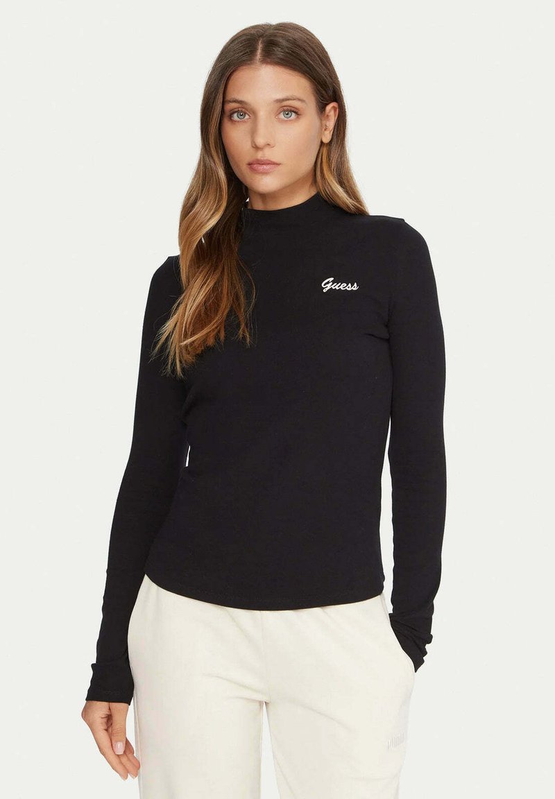 Top nero a maniche lunghe realizzato in tessuto morbido, con collo alto, silhouette aderente e logo bianco "Guess" sul petto a sinistra.