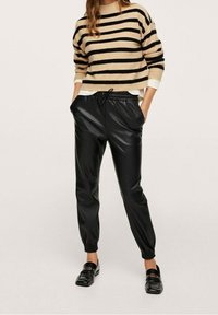 Beige en zwart gestreepte trui, losse pasvorm, gecombineerd met zwarte faux leren joggers met elastische boorden en een drawstring taille. Zwarte loafers.